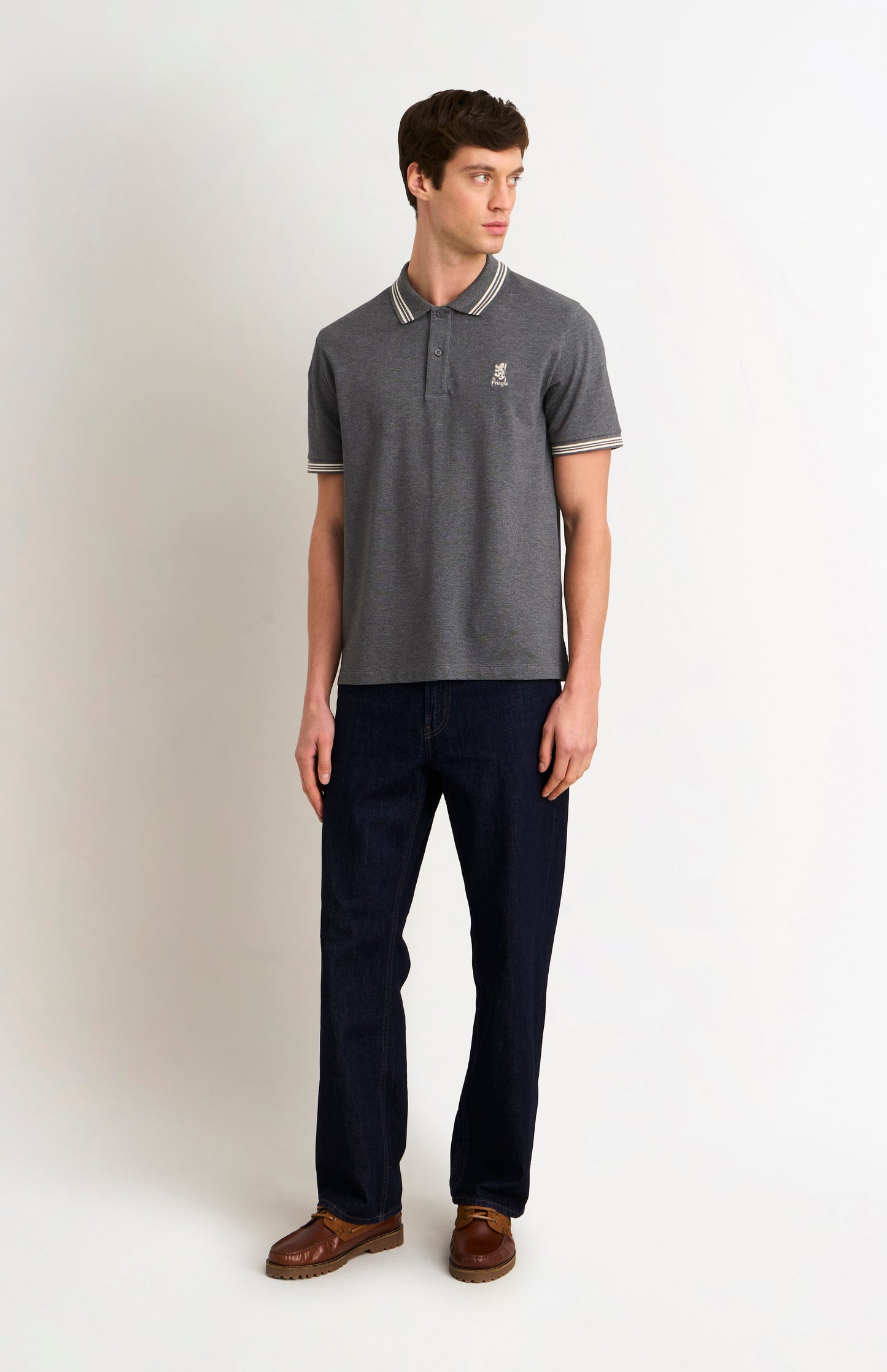 Full body shot of a model wearing a charcoal grey polo with white tipping details and a Pringle logo on the upper side of the chest