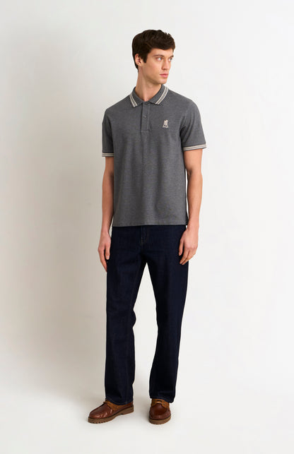 Full body shot of a model wearing a charcoal grey polo with white tipping details and a Pringle logo on the upper side of the chest