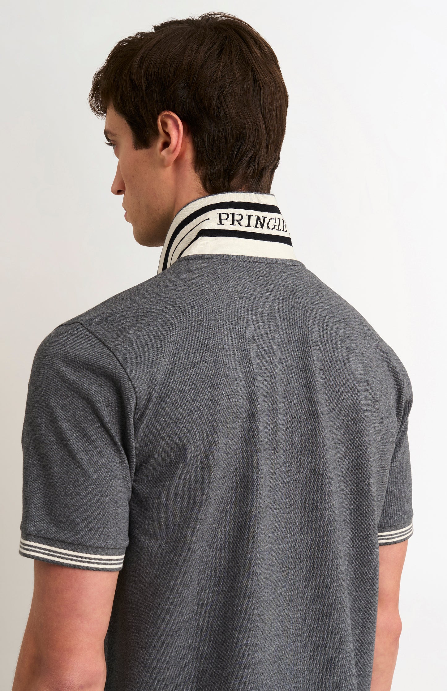 Model wearing a charcoal grey polo with white tipping details and PRINGLE under the flipped-up collar