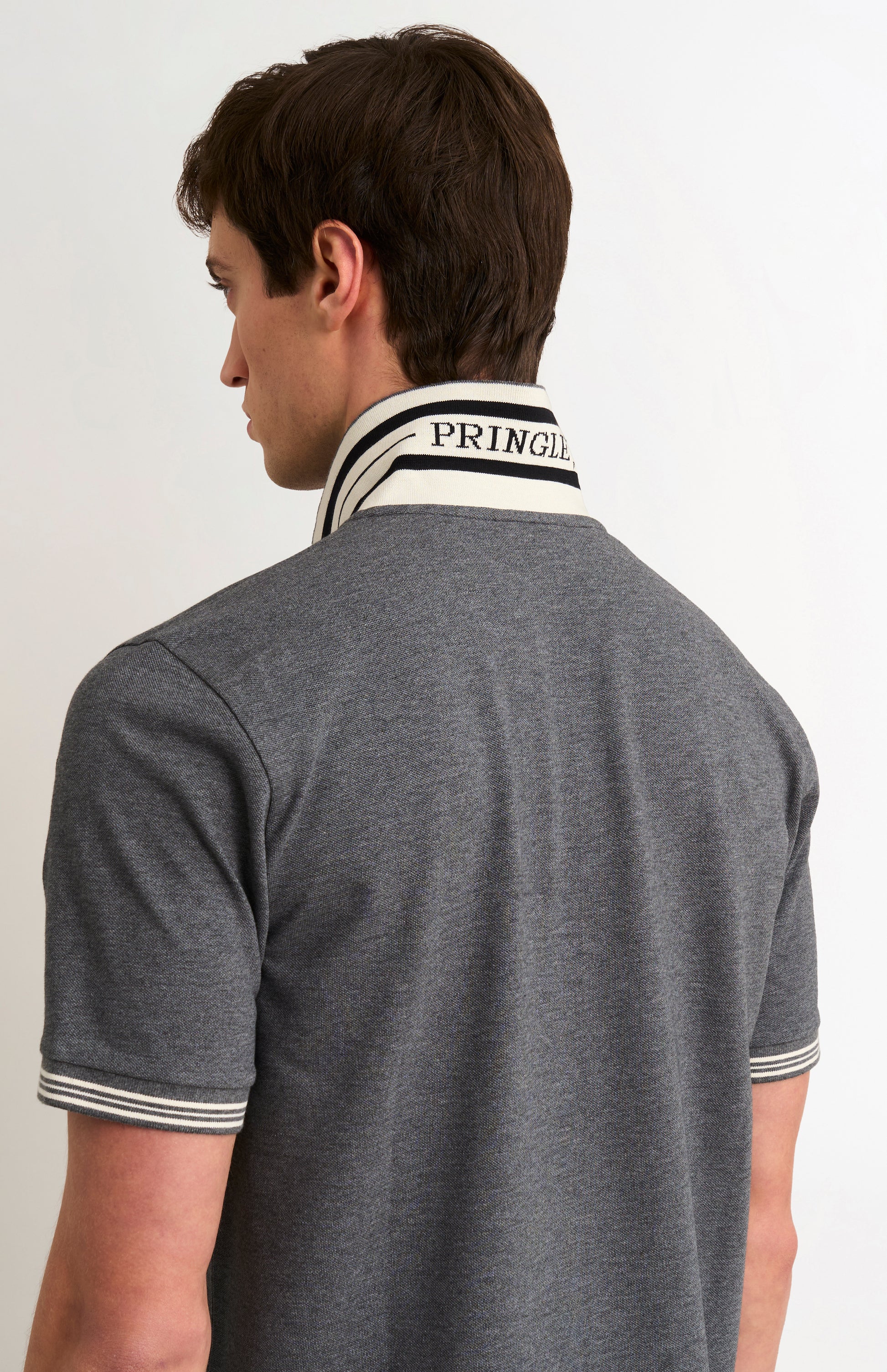 Model wearing a charcoal grey polo with white tipping details and PRINGLE under the flipped-up collar