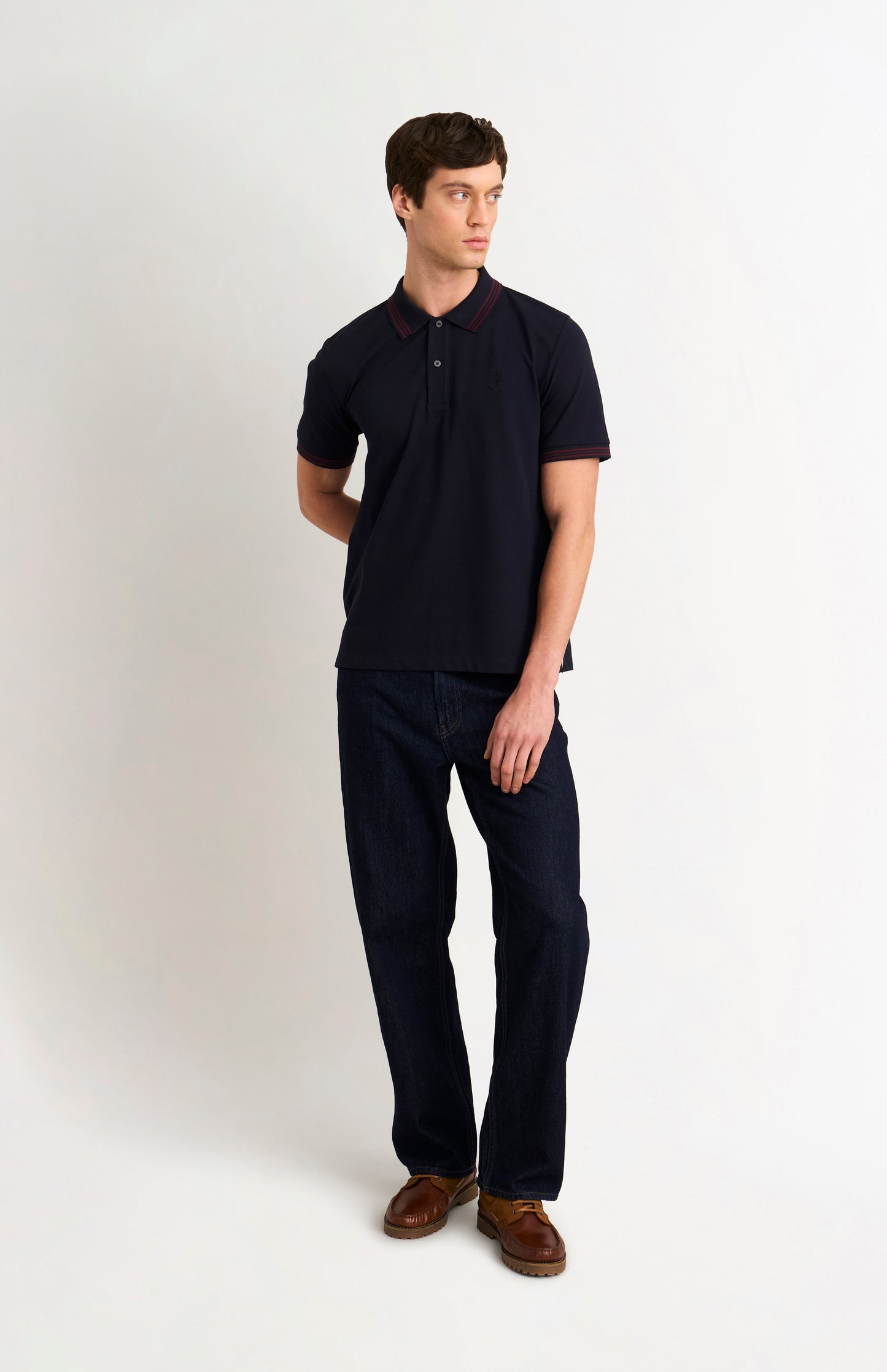 Full body shot of model wearing a navy polo shirt with burgundy tipping details and Pringle logo on upper side of chest