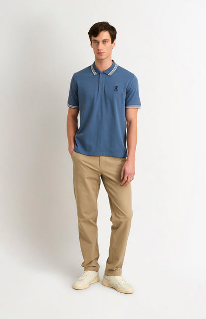 Full body shot of model wearing a mid blue polo with tipping details and Pringle logo on upper side of chest