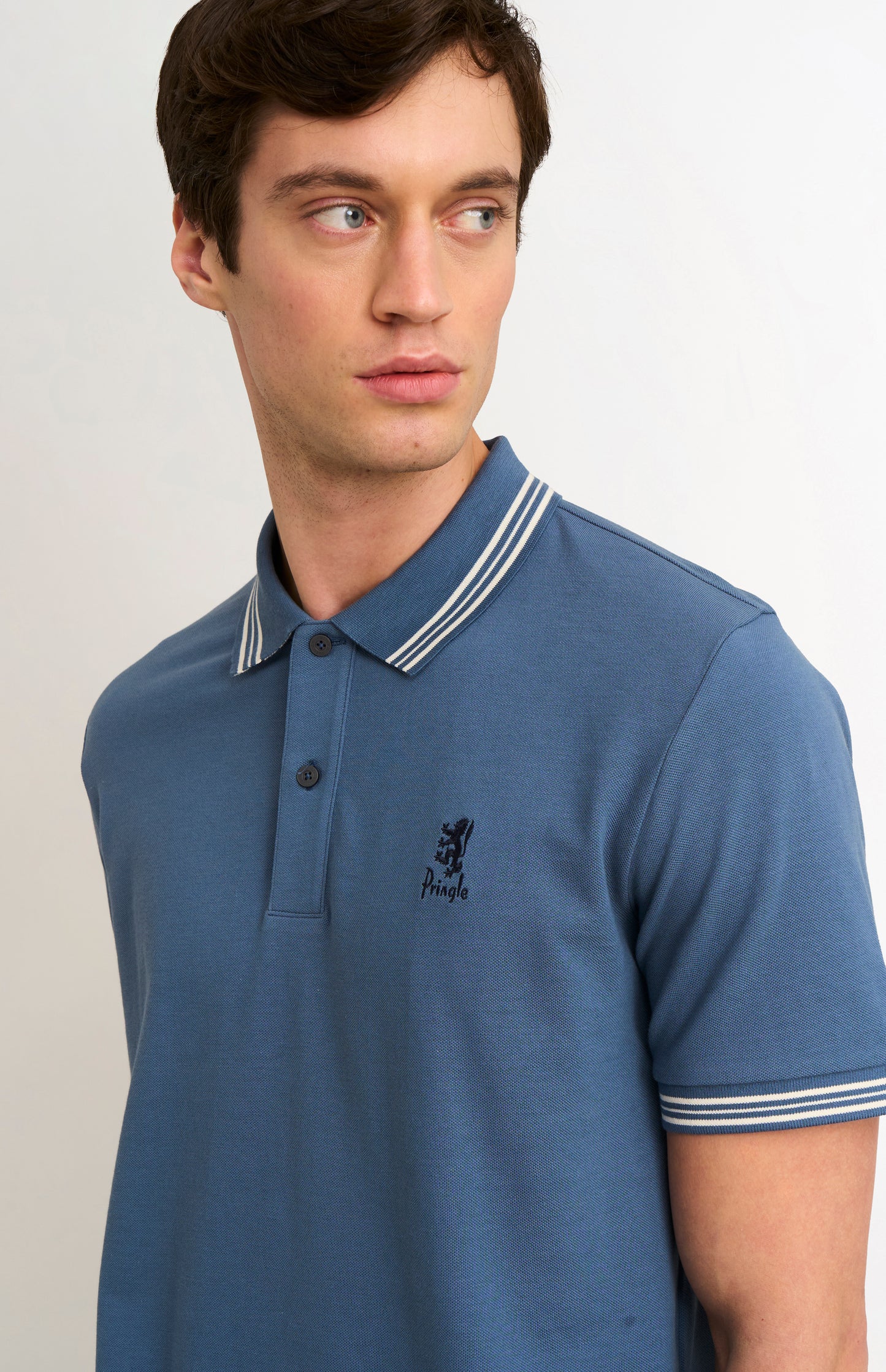Man wearing a mid blue polo with tipping details and Pringle logo on upper side of chest
