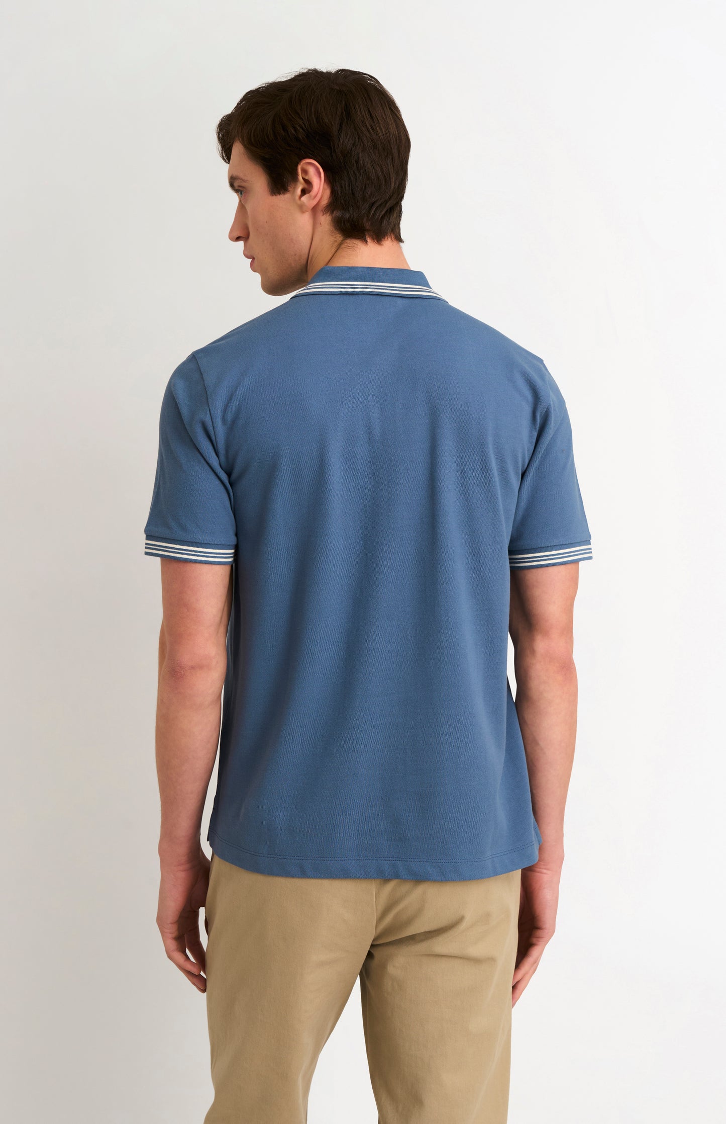Photo from the back of model wearing a mid blue polo with tipping details