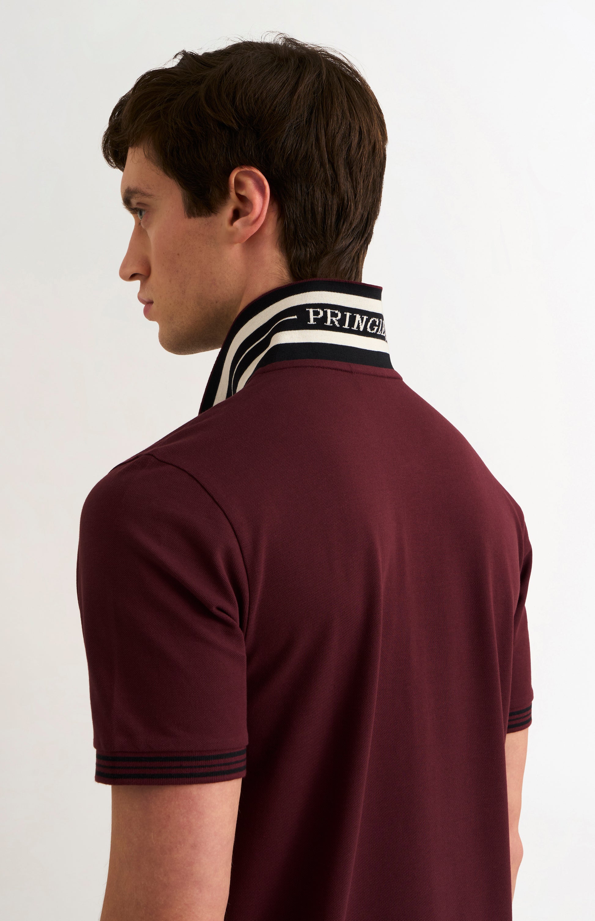 Detail shot of a model wearing a burgundy polo with PRINGLE underneath the flipped-up collar