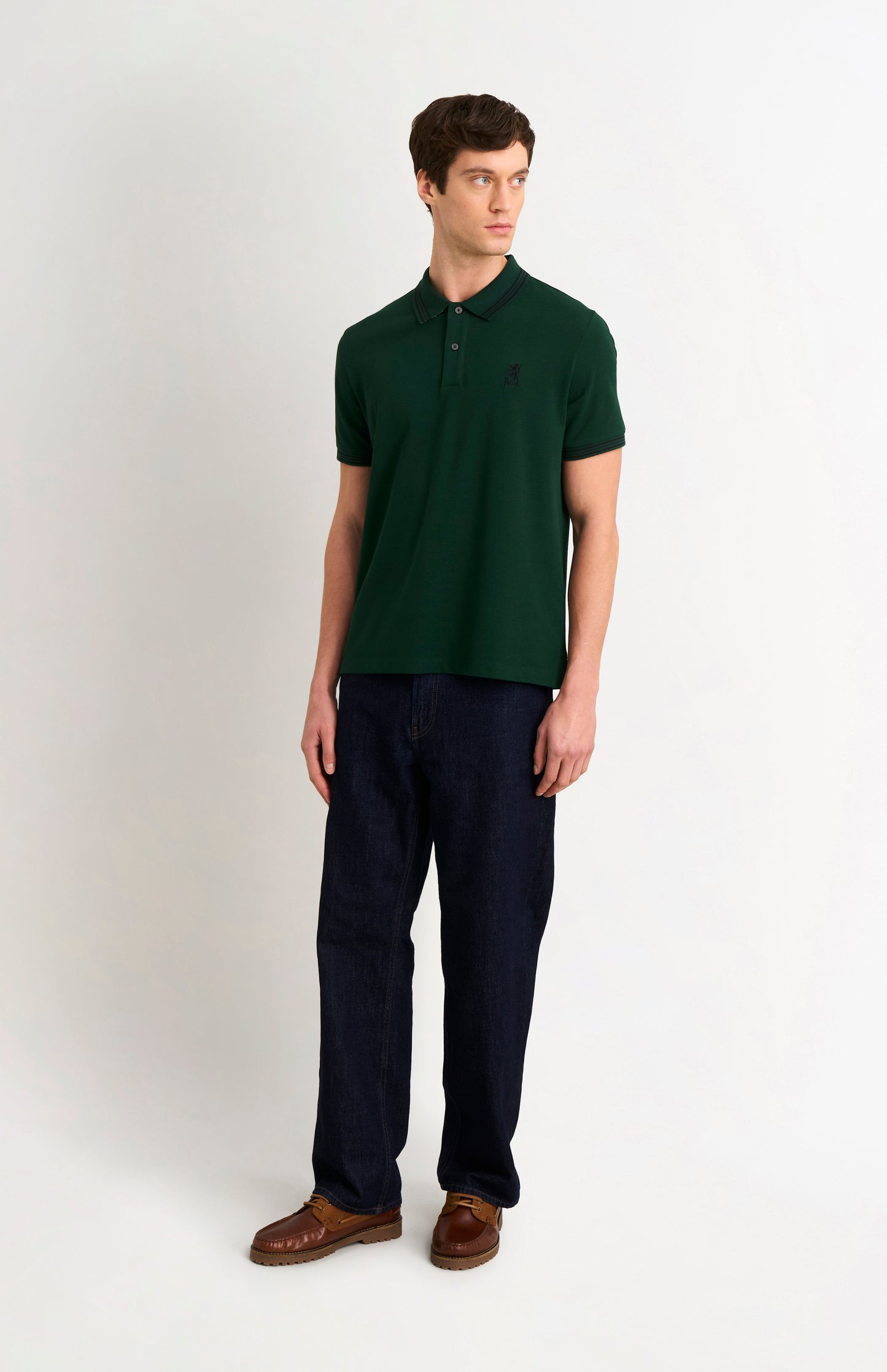 Model wearing a forest green polo with tipping details and small Pringle logo on upper side of chest, and dark trousers