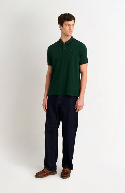 Model wearing a forest green polo with tipping details and small Pringle logo on upper side of chest, and dark trousers