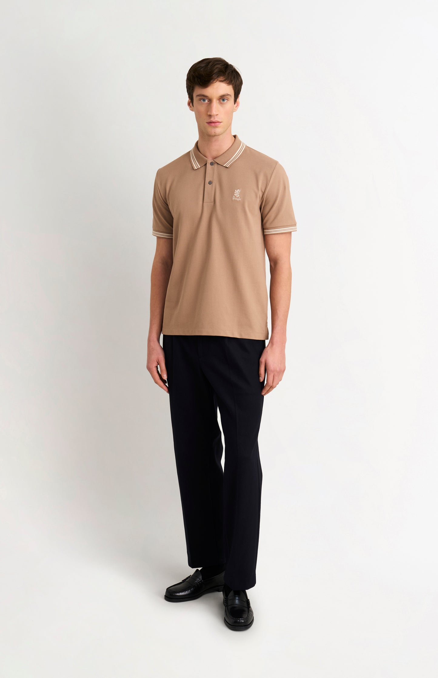 Full body shot of model wearing a mushroom light brown polo with tipping and Pringle logo on upper side of chest