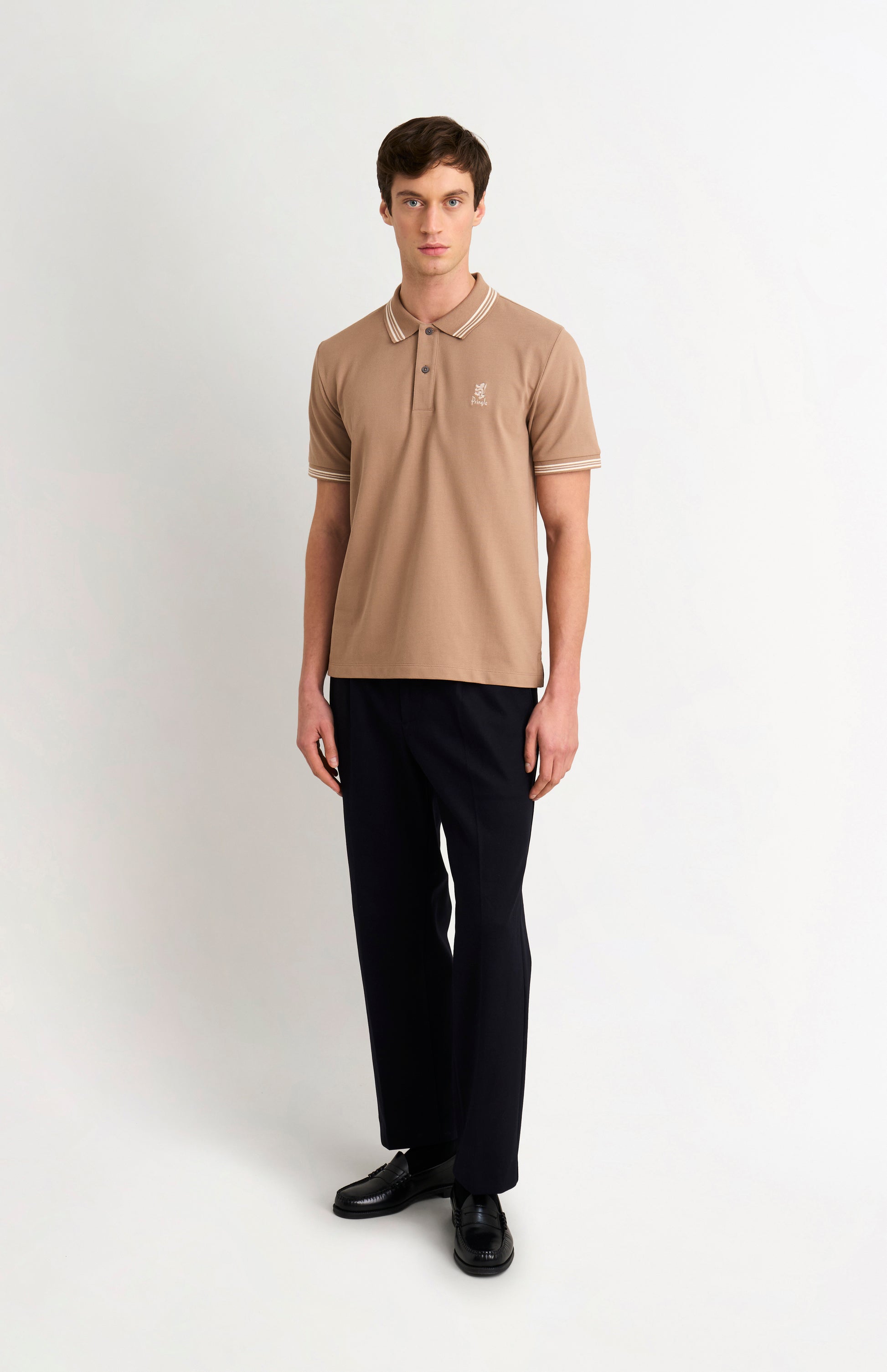 Full body shot of model wearing a mushroom light brown polo with tipping and Pringle logo on upper side of chest