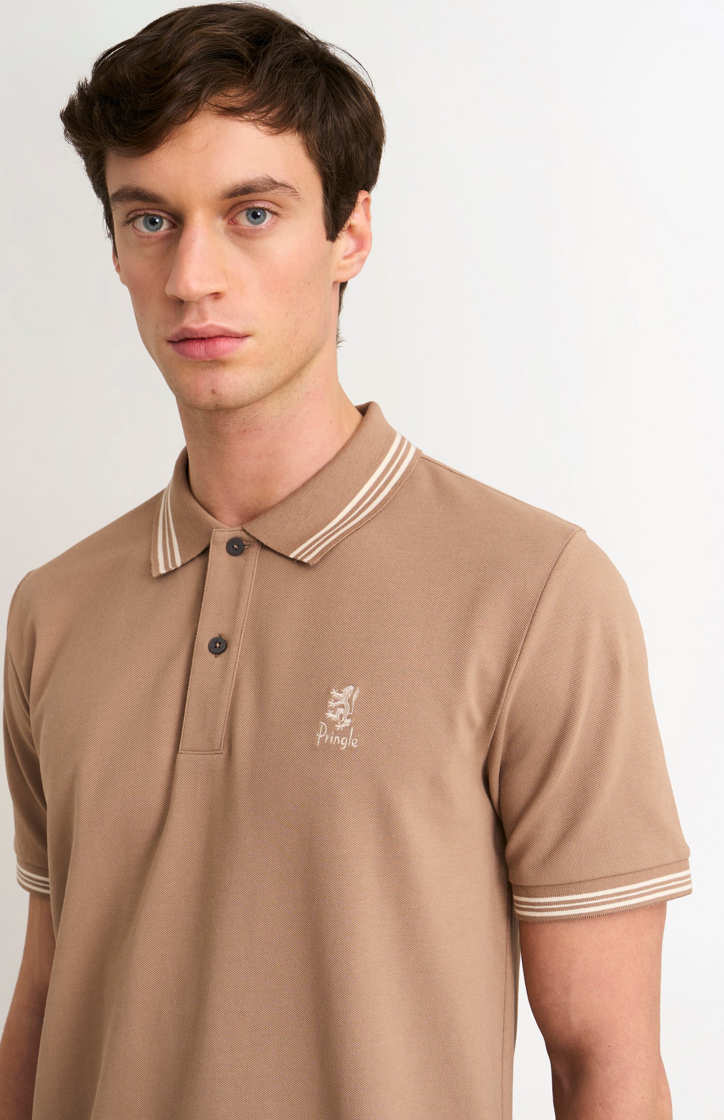 Close-up shot of model wearing a mushroom light brown polo with tipping and Pringle logo on upper side of chest