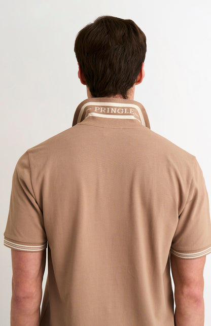 Model wearing a mushroom light brown polo with tipping and PRINGLE written under the flipped-up collar