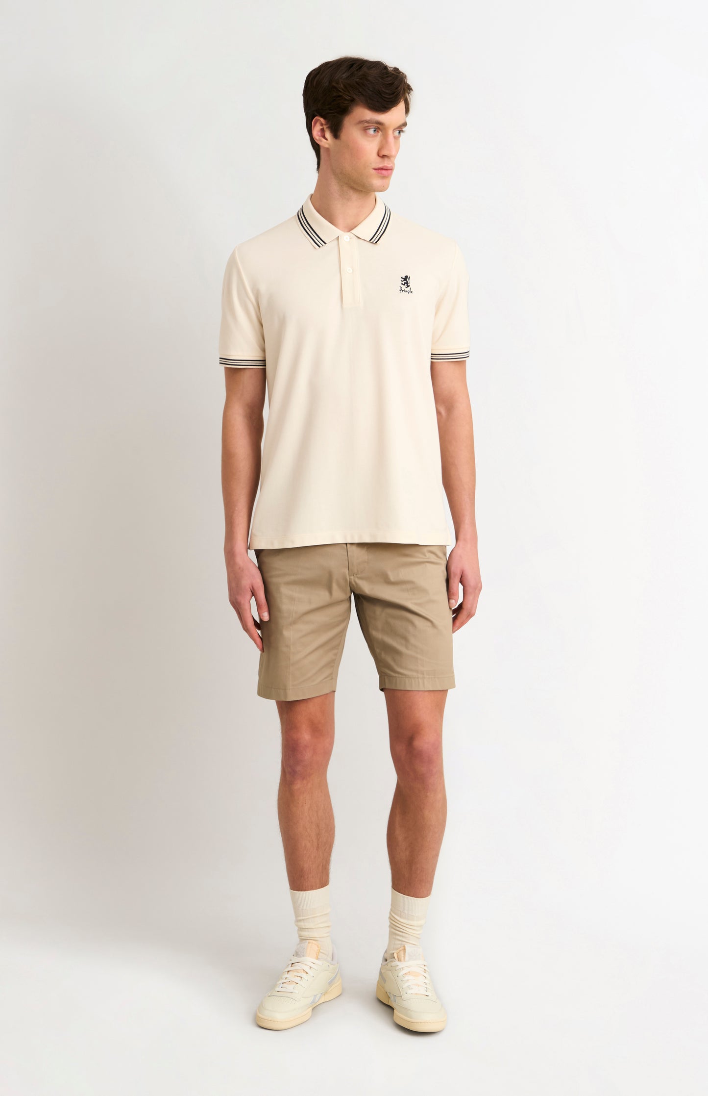 Man wearing a cream polo shirt and beige shorts on a white background
