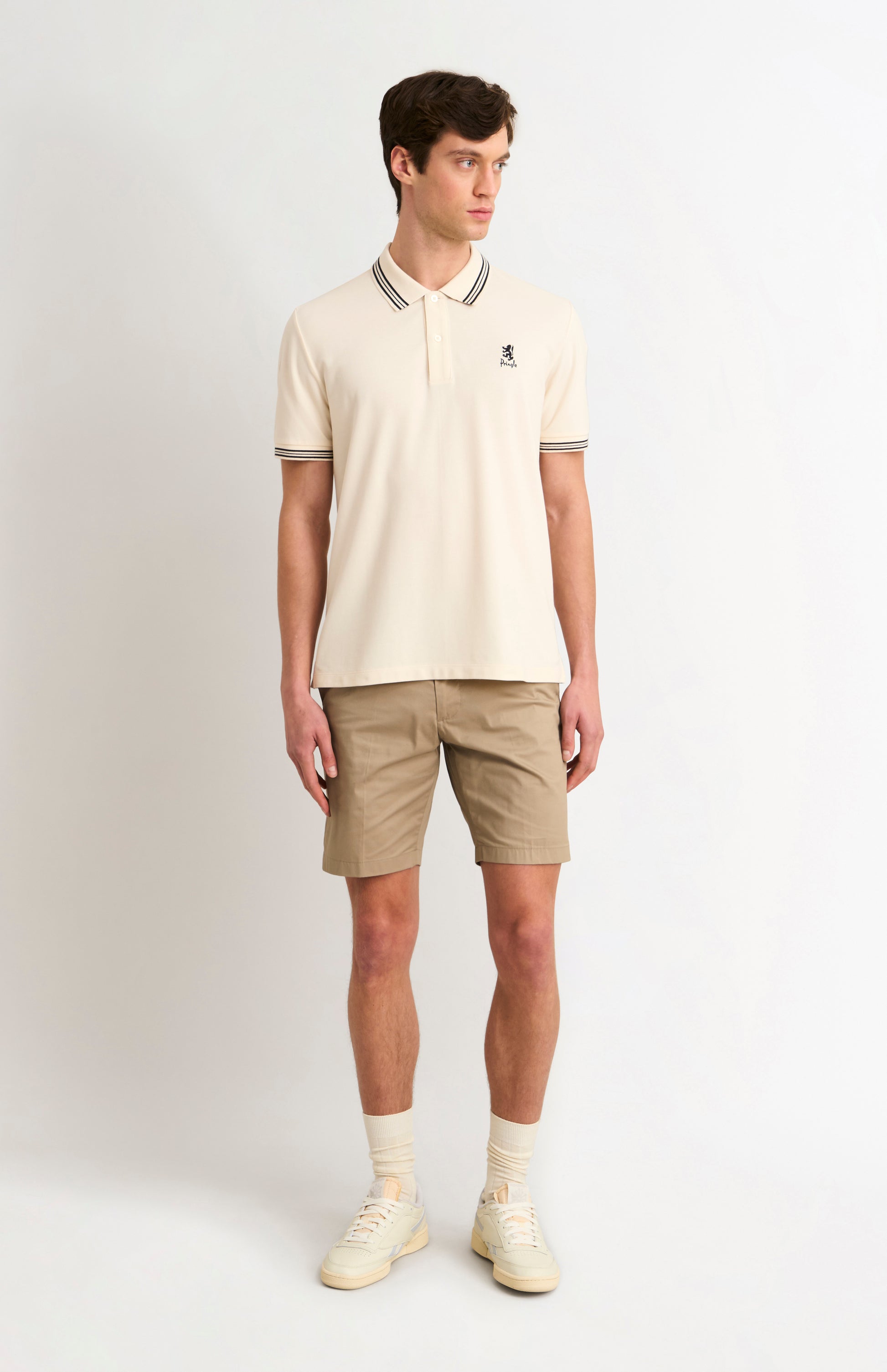 Man wearing a cream polo shirt and beige shorts on a white background