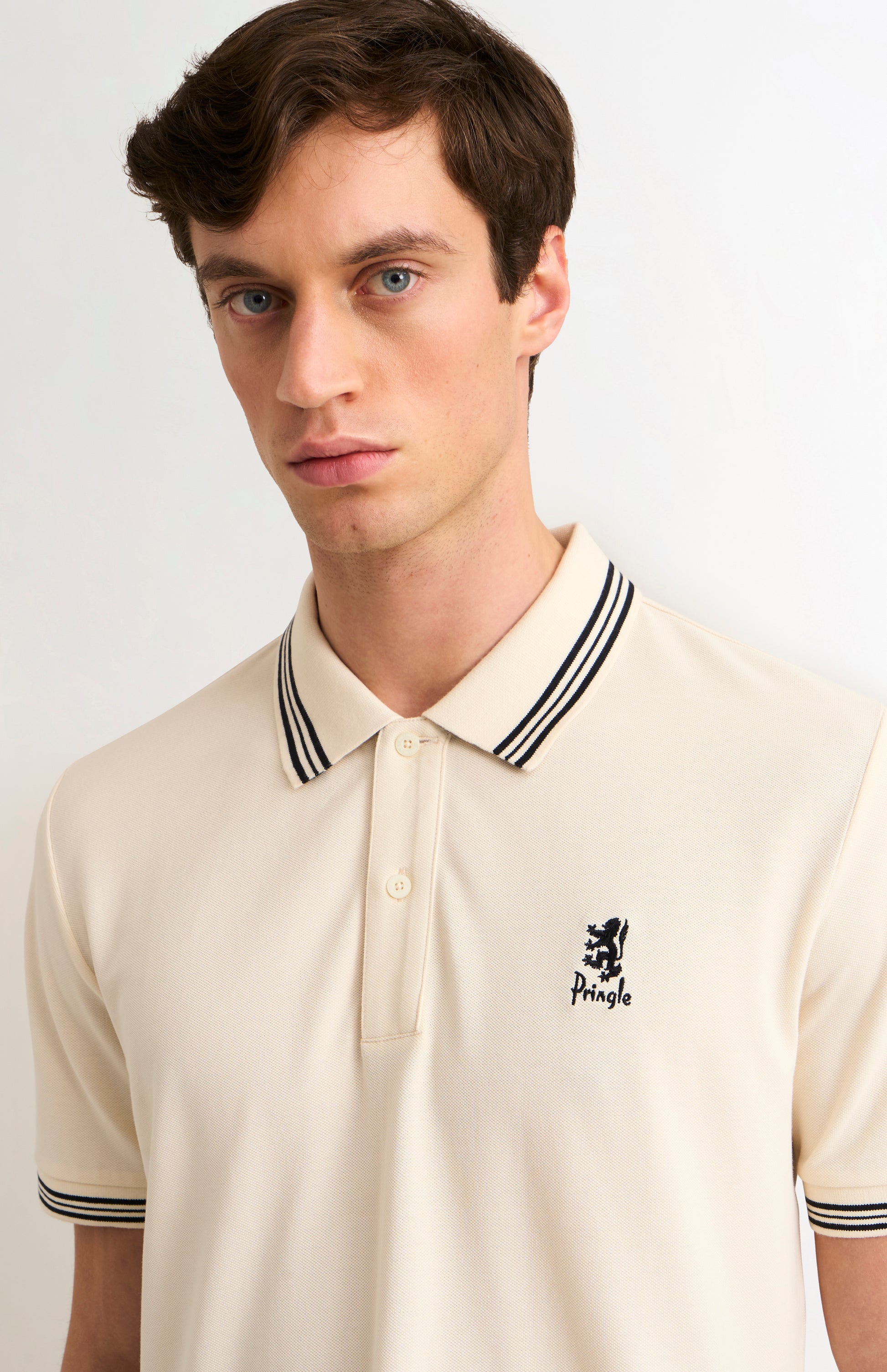Man wearing a beige polo shirt with black and white trim on a light background