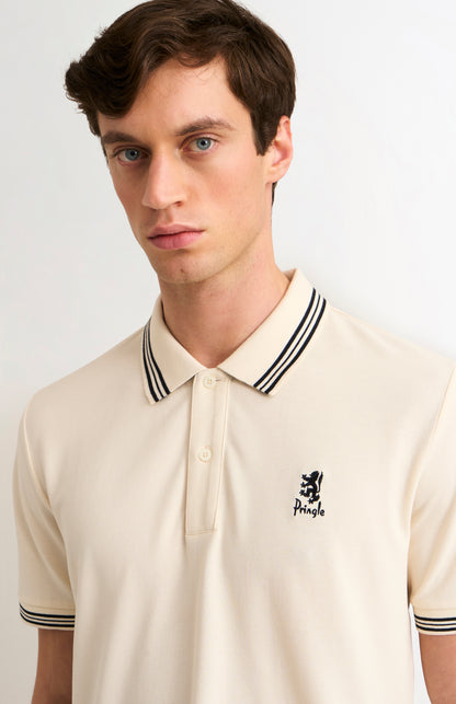 Man wearing a beige polo shirt with black and white trim on a light background