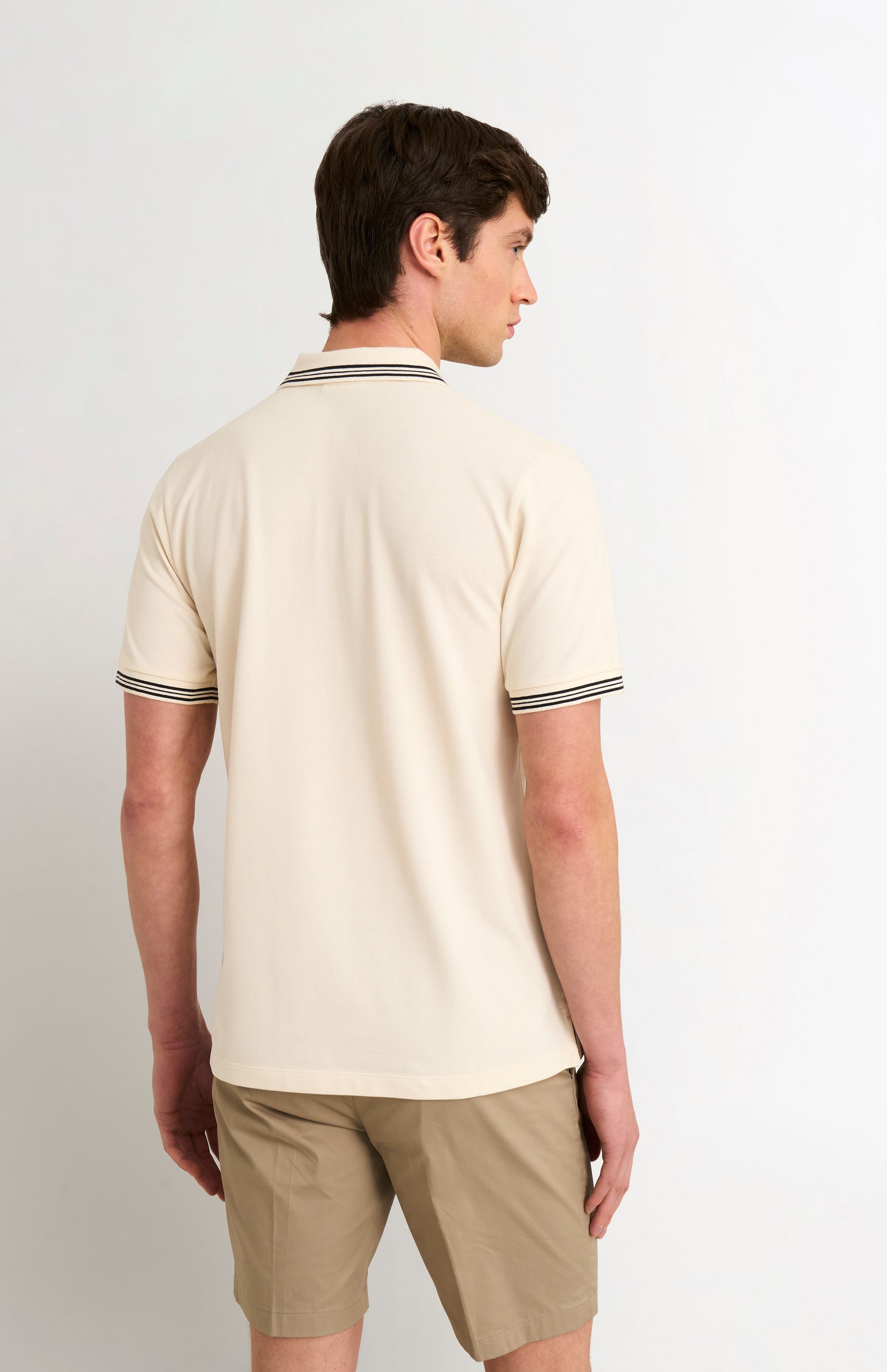 Man wearing a beige polo shirt and shorts on a white background