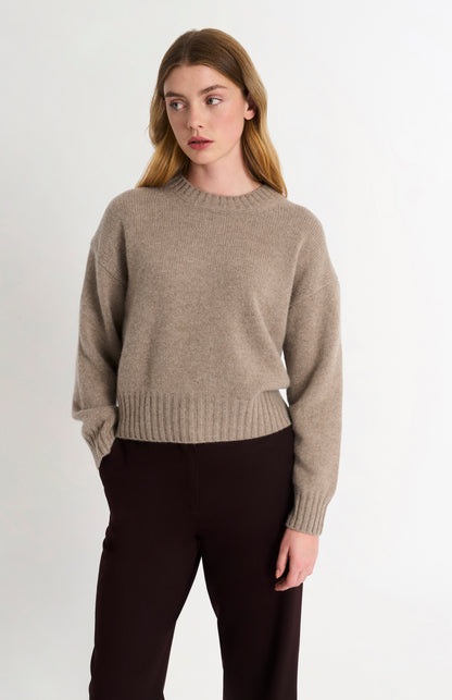 Woman wearing a beige sweater and black pants on a white background