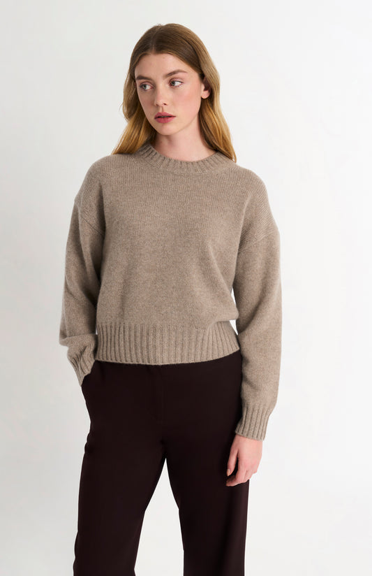 Woman wearing a beige sweater and black pants on a white background